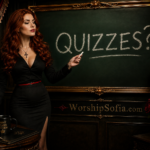 Goddess Sofia, a regal auburn-haired woman in a fitted black blouse and pencil skirt, stands beside an ornate old-fashioned green chalkboard writing “QUIZZES?!” in white chalk. Rich dark wood, crimson velvet curtains, candlelight, gold detailing, antique books, and roses surround her. WorshipSofia.com appears below.